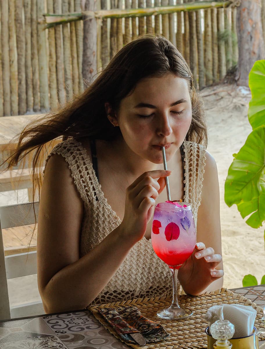 Moça com camiza de crochê bebendo um drink vermelho com canudinho